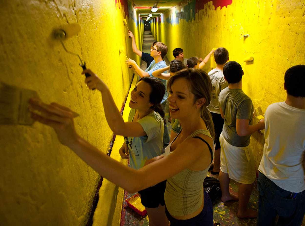 Students painting over graffiti walls in tunnels at University of Rochester